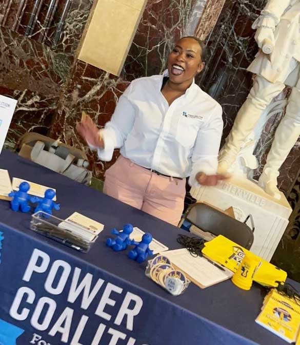 A young black woman exclaims excitedly behind a table for the Power Coalition for Equity and Justice